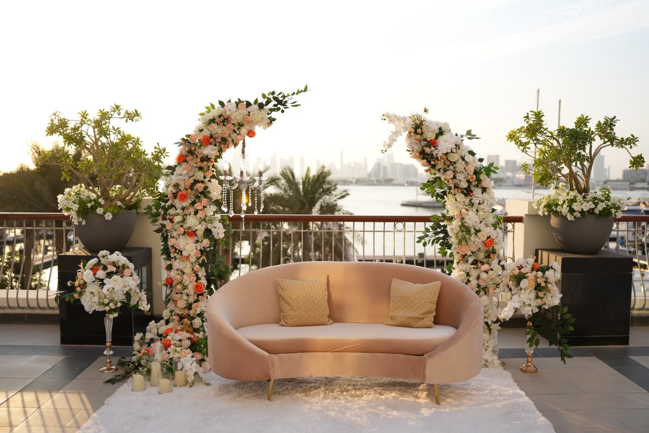 Waterfront wedding lounge with a blush velvet sofa and floral arches overlooking the Dubai marina